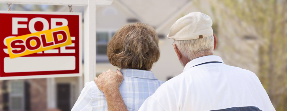 Senior man and woman look at their home which has a sold real estate sign in front of it